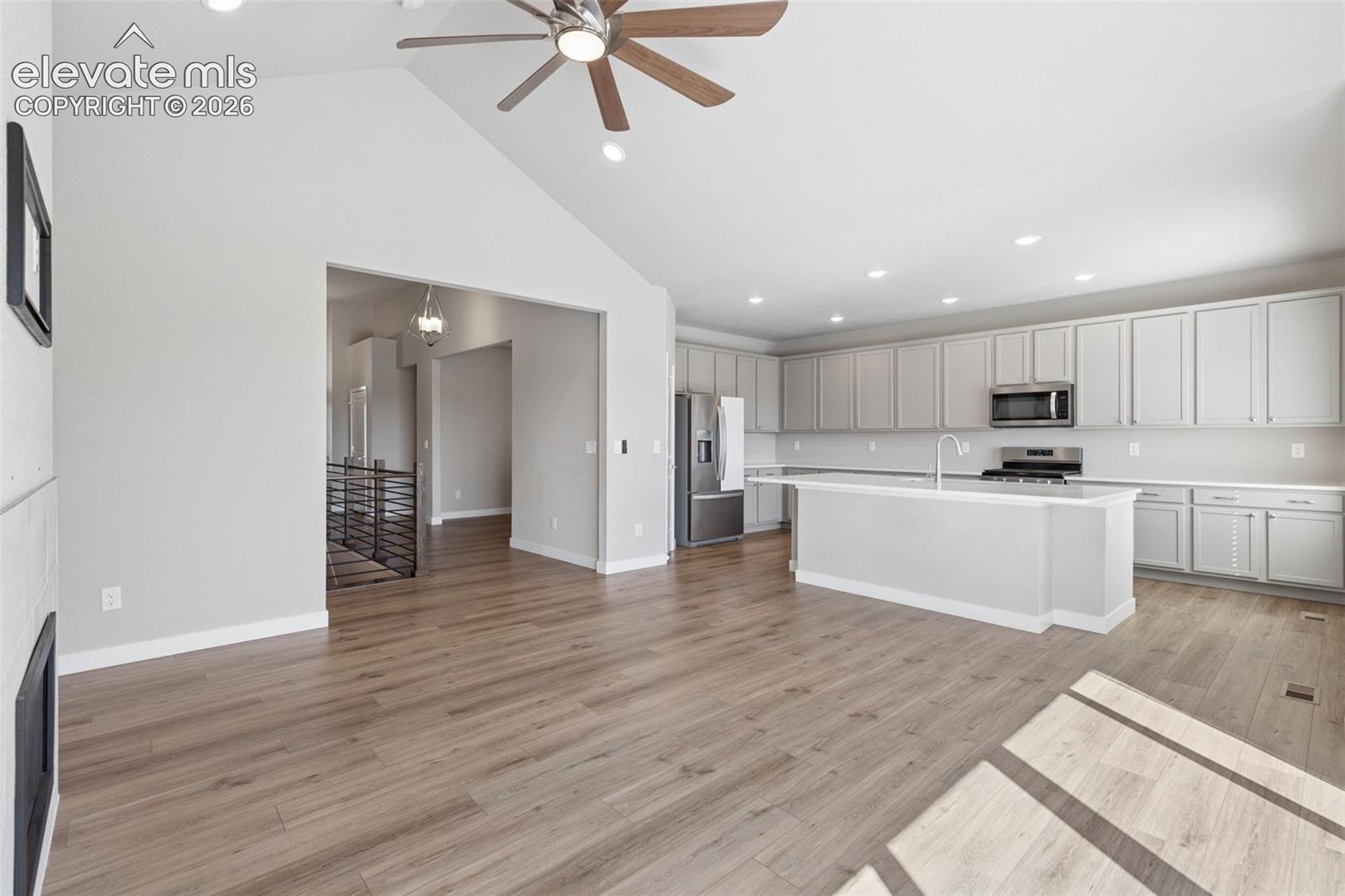 Vaulted ceiling with an integrated ceiling fan, wood-finish flooring, recessed lighting, and a kitchen featuring cabinetry with an island