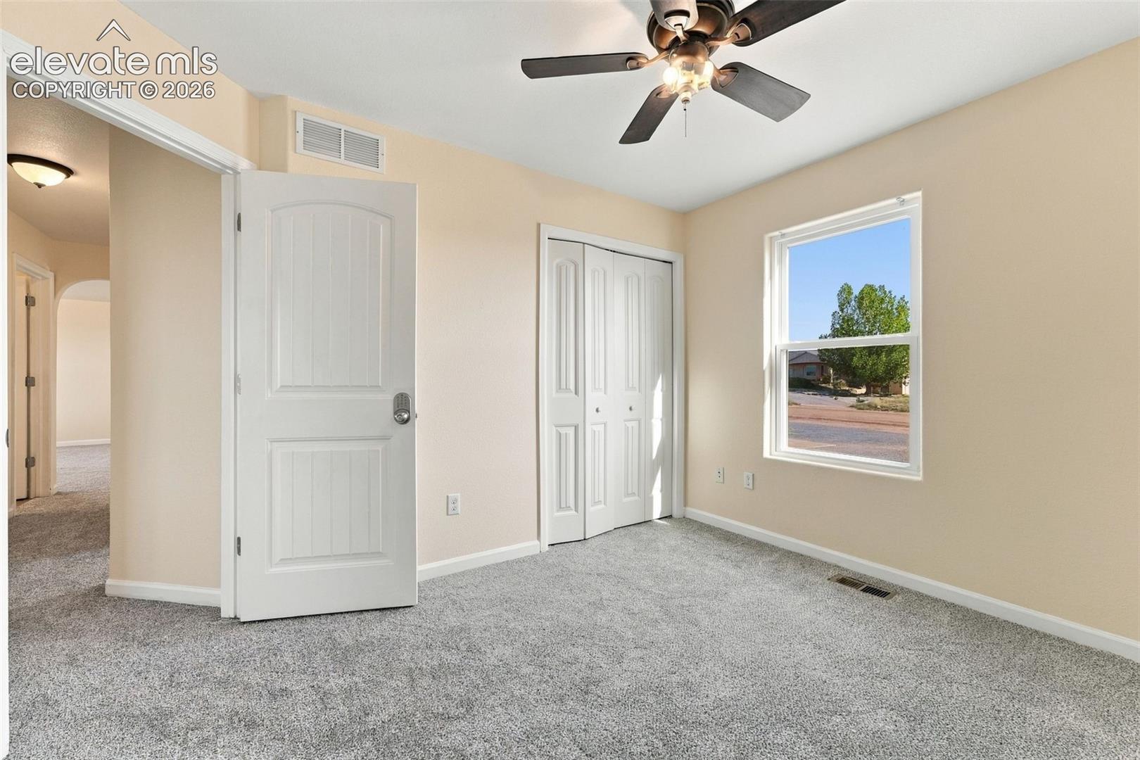 Neutral-toned bedroom featuring carpeting, a multi-panel door, a bi-fold closet, and a ceiling fan with integrated lighting