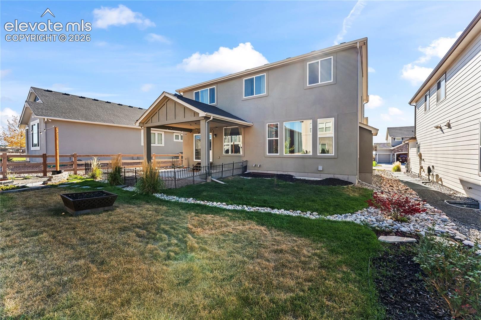 Rear exterior featuring a covered patio, fenced yard with rock landscaping, and stucco siding