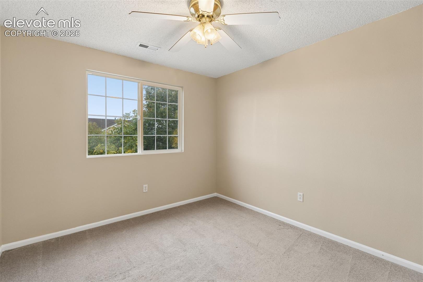 Neutral-toned interior space featuring wall-to-wall carpeting, a multi-pane sliding window, and a central ceiling fan with an integrated three-light fixture