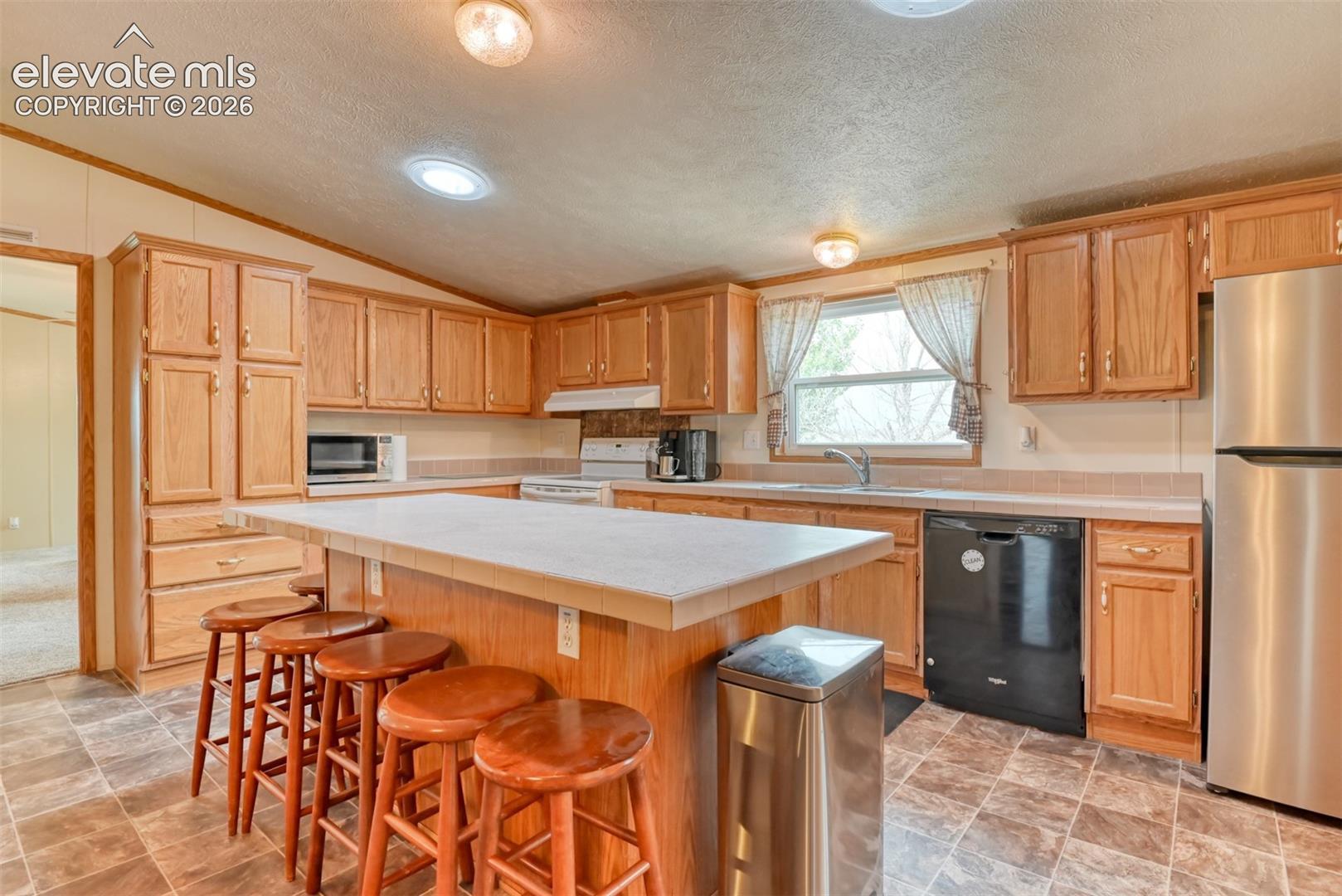 Kitchen featuring wood cabinetry, a central island with countertop, a stainless steel refrigerator, and tiled flooring
