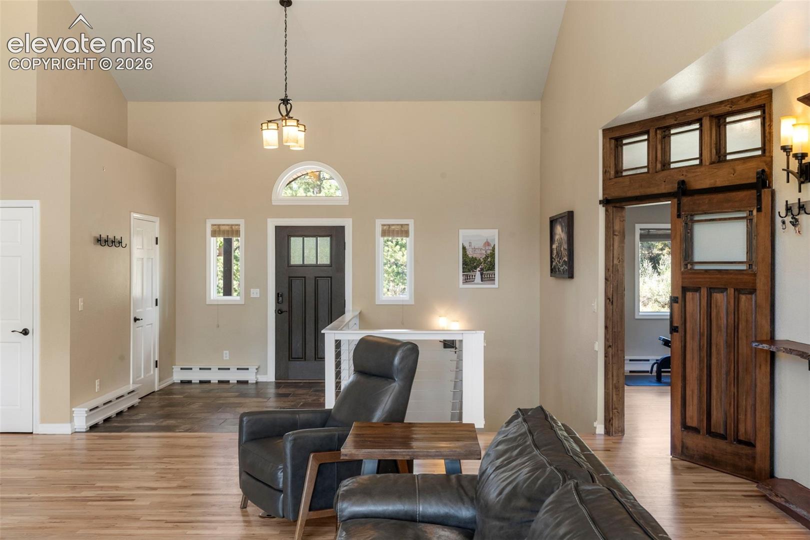 Foyer entrance featuring high vaulted ceiling, light wood-style floors, a barn door, and a baseboard heating unit