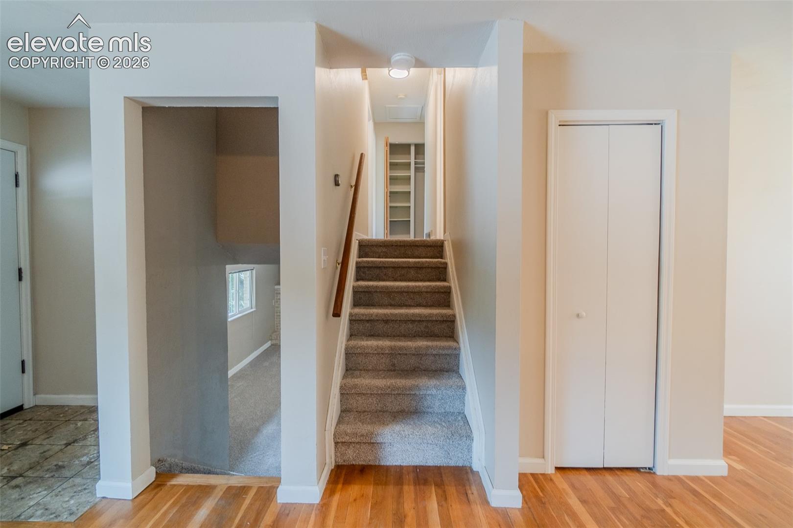 Hardwood flooring, carpeted staircase with wood handrail, white trim, and bi-fold closet doors