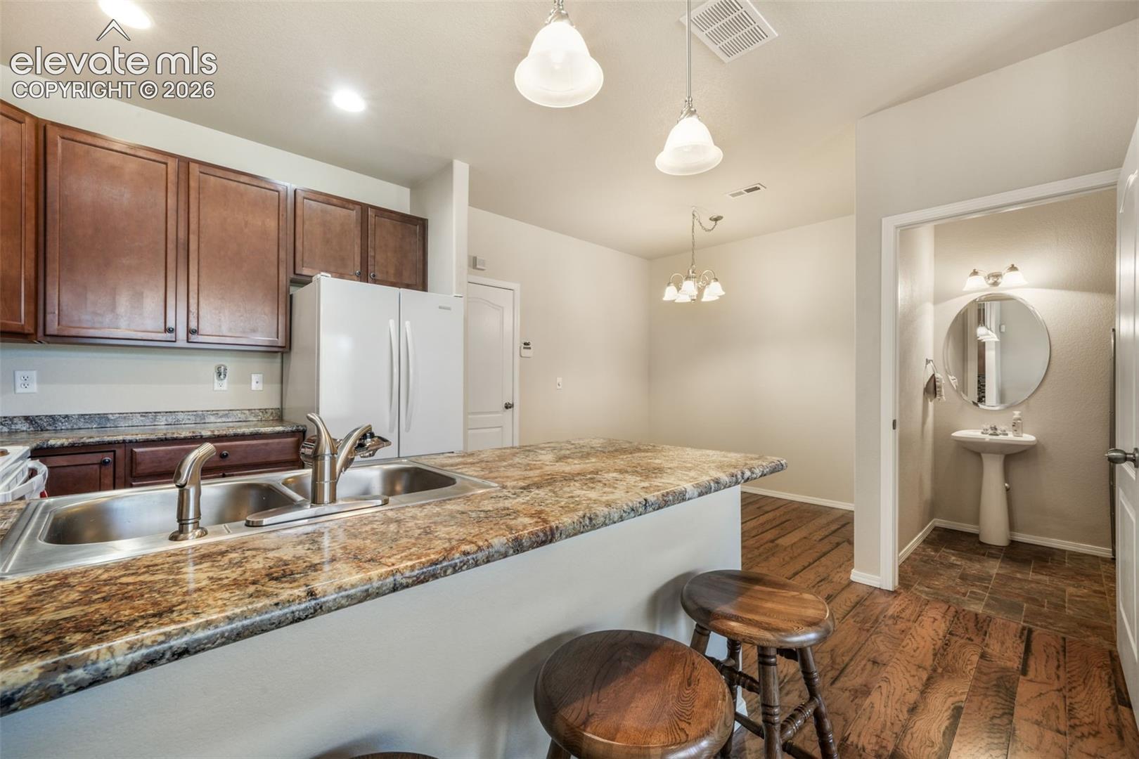 Kitchen featuring wood-finish cabinetry, a stainless steel double basin sink, and a stone-look countertop with an overhang