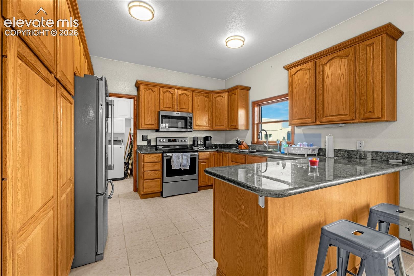 Kitchen featuring wood cabinetry, dark countertops, a window over the sink, and tile flooring