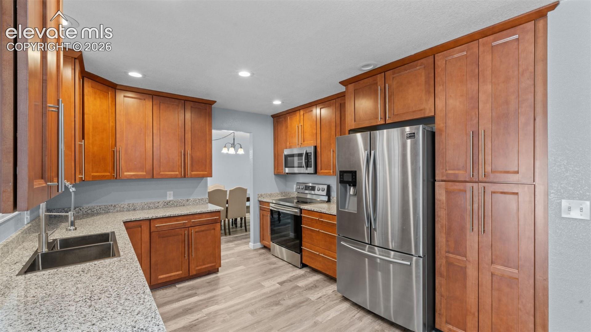 Kitchen featuring wood-finish cabinetry, light-toned countertops, stainless steel appliances, and recessed lighting