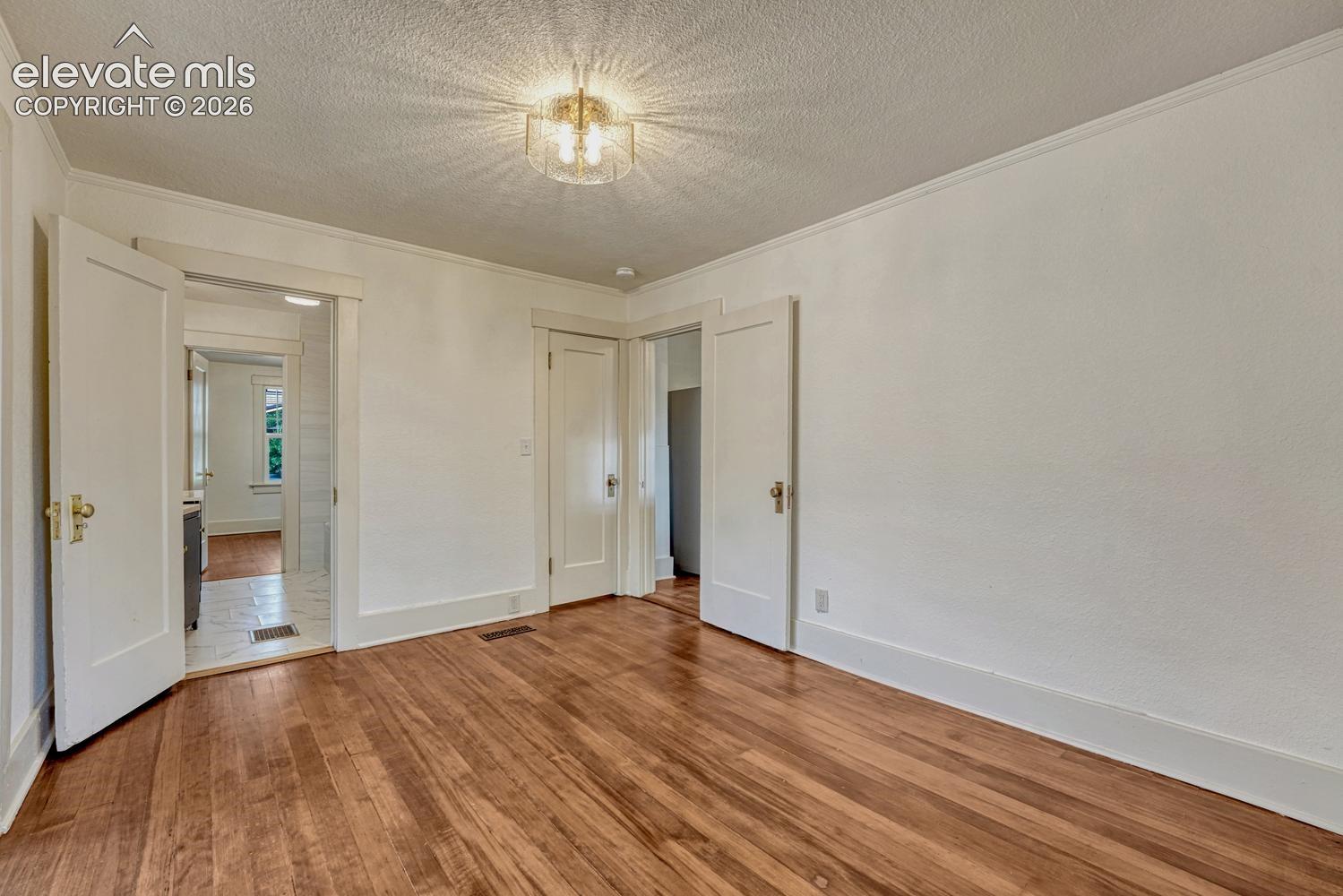 Hardwood flooring, crown molding, white trim, recessed door frame, and a contemporary ceiling light fixture