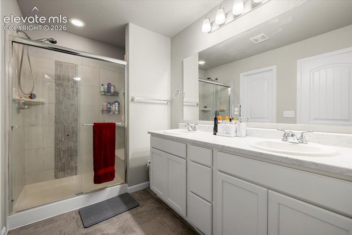 Dual vanity with integrated sinks, framed mirror, and a glass-enclosed shower featuring a tiled accent stripe