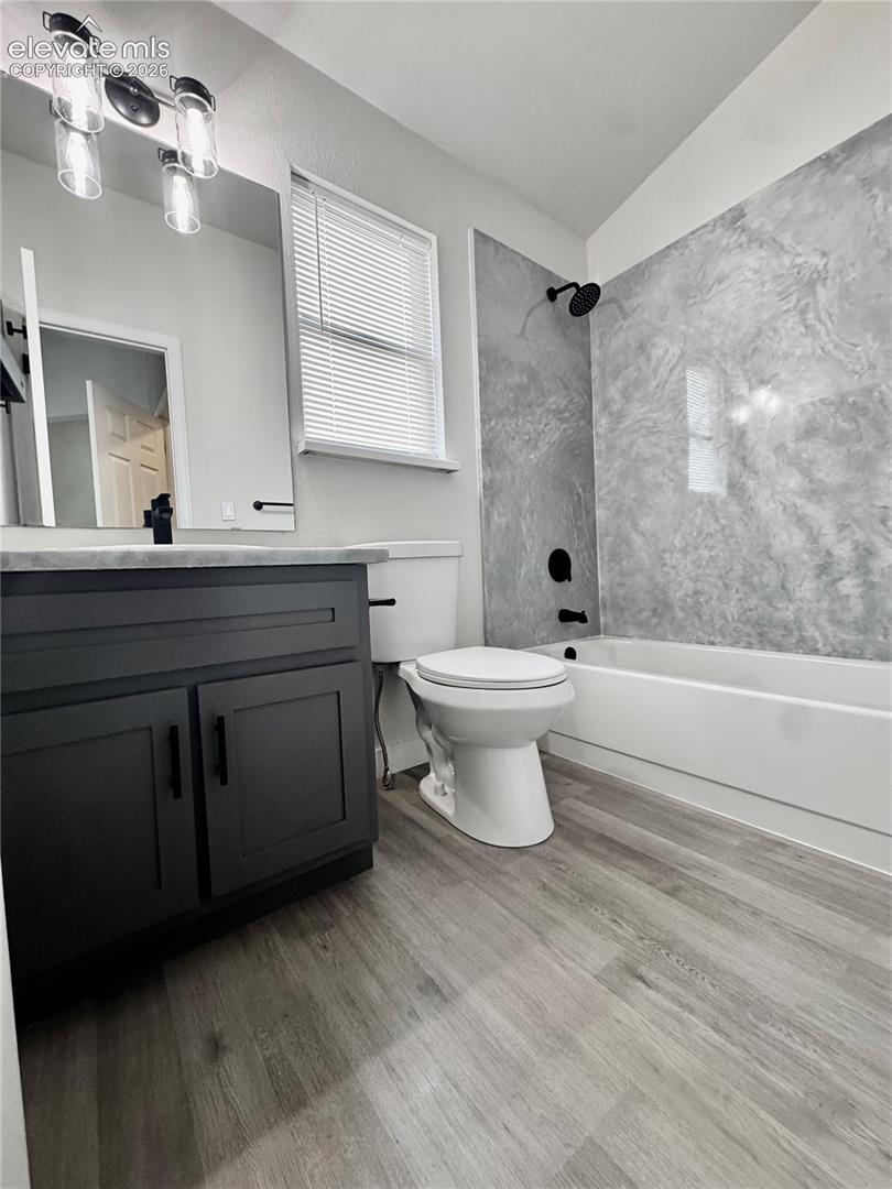 Wood-finish flooring, dark vanity with black hardware, and a tub/shower combination with a textured wall surround