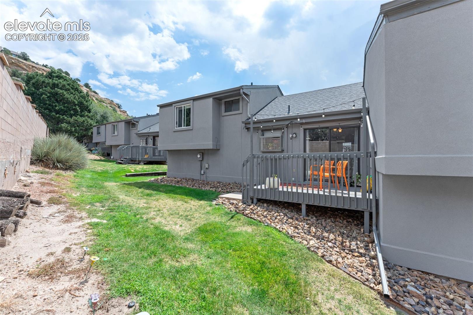 Private exterior deck with a sliding glass door, accompanied by an expansive grassy area and a rock border