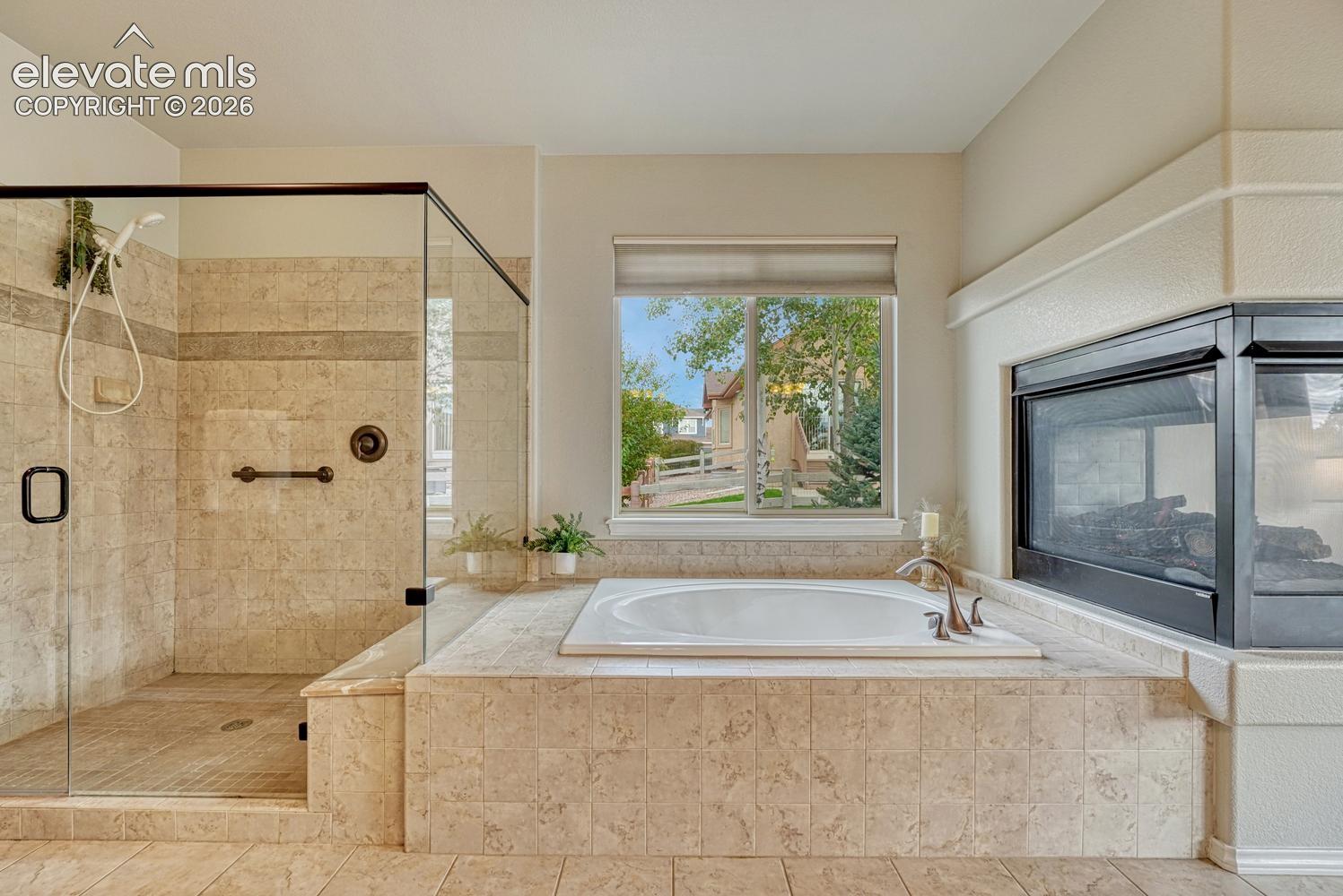 Luxurious 5-piece Primary Bathroom with 3-sided fireplace, soaking tub, and separate large tiled shower with built-in bench and grab bar.