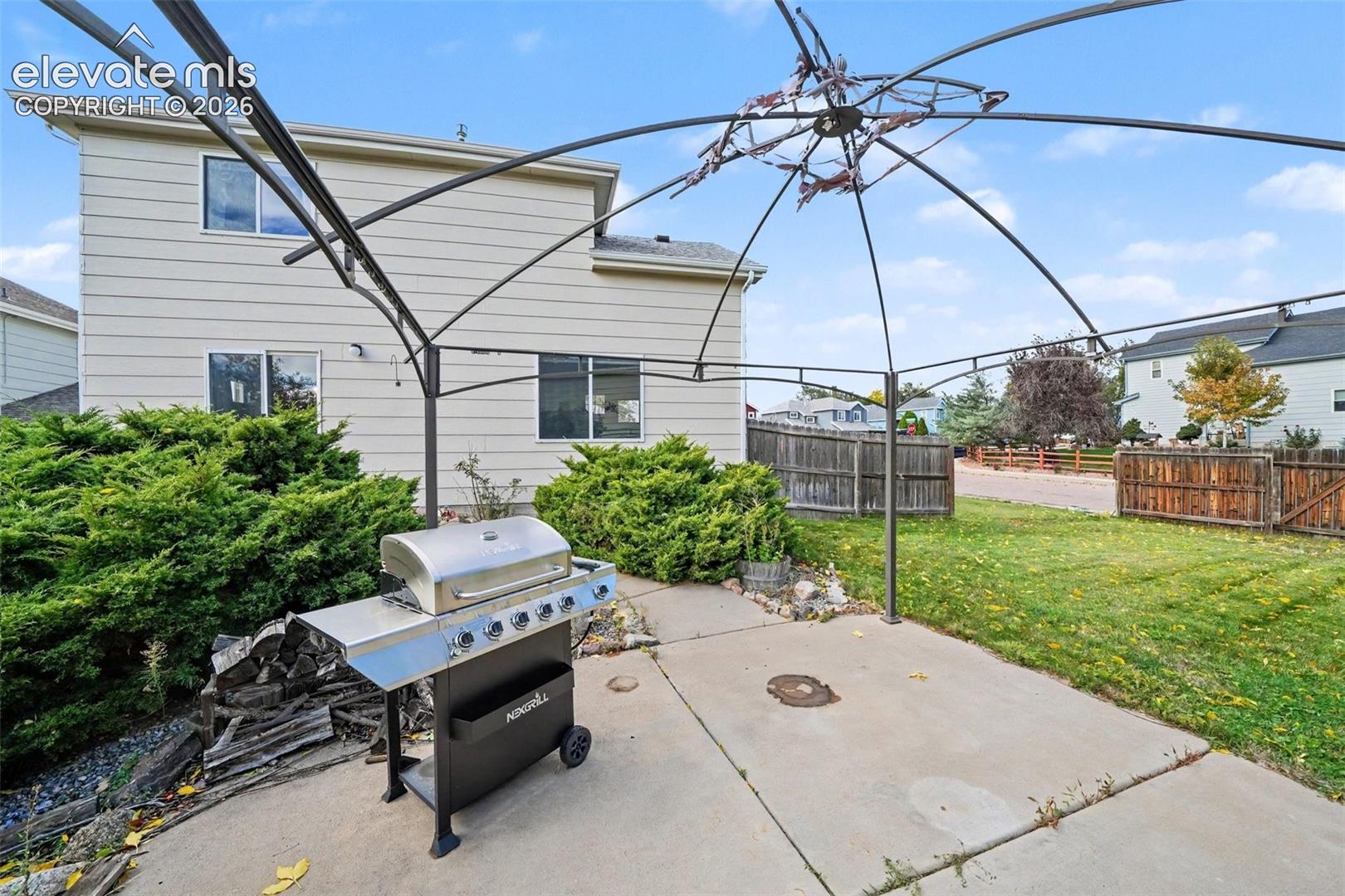 Rear yard featuring a concrete patio, metal gazebo frame, and wood perimeter fencing