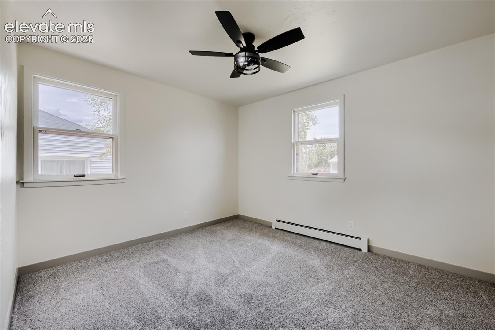 Bright, light-filled bedroom with dual windows providing natural illumination, neutral wall finishes, and carpeted flooring