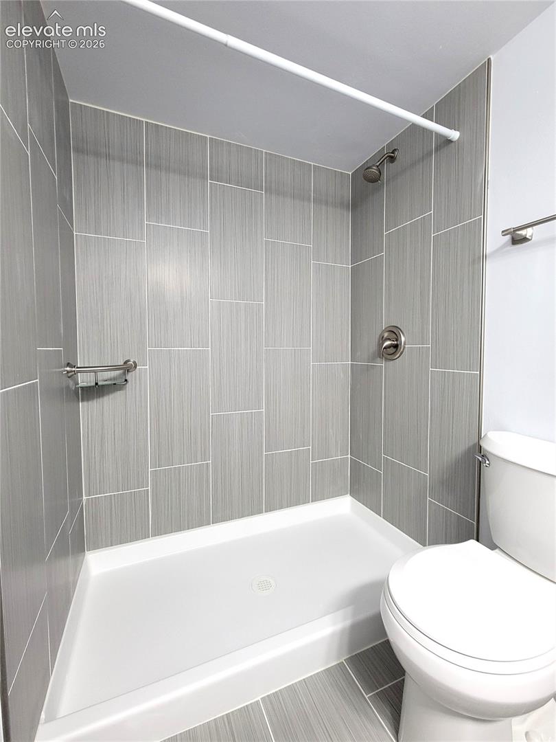 Walk-in shower featuring light grey vertical plank tile, brushed nickel fixtures, and an integrated soap dish