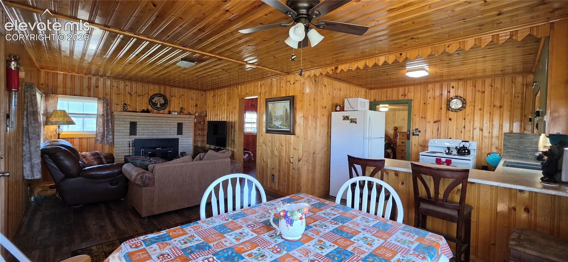 Wood-paneled interior featuring a brick fireplace, wood-finish flooring, and a ceiling fan