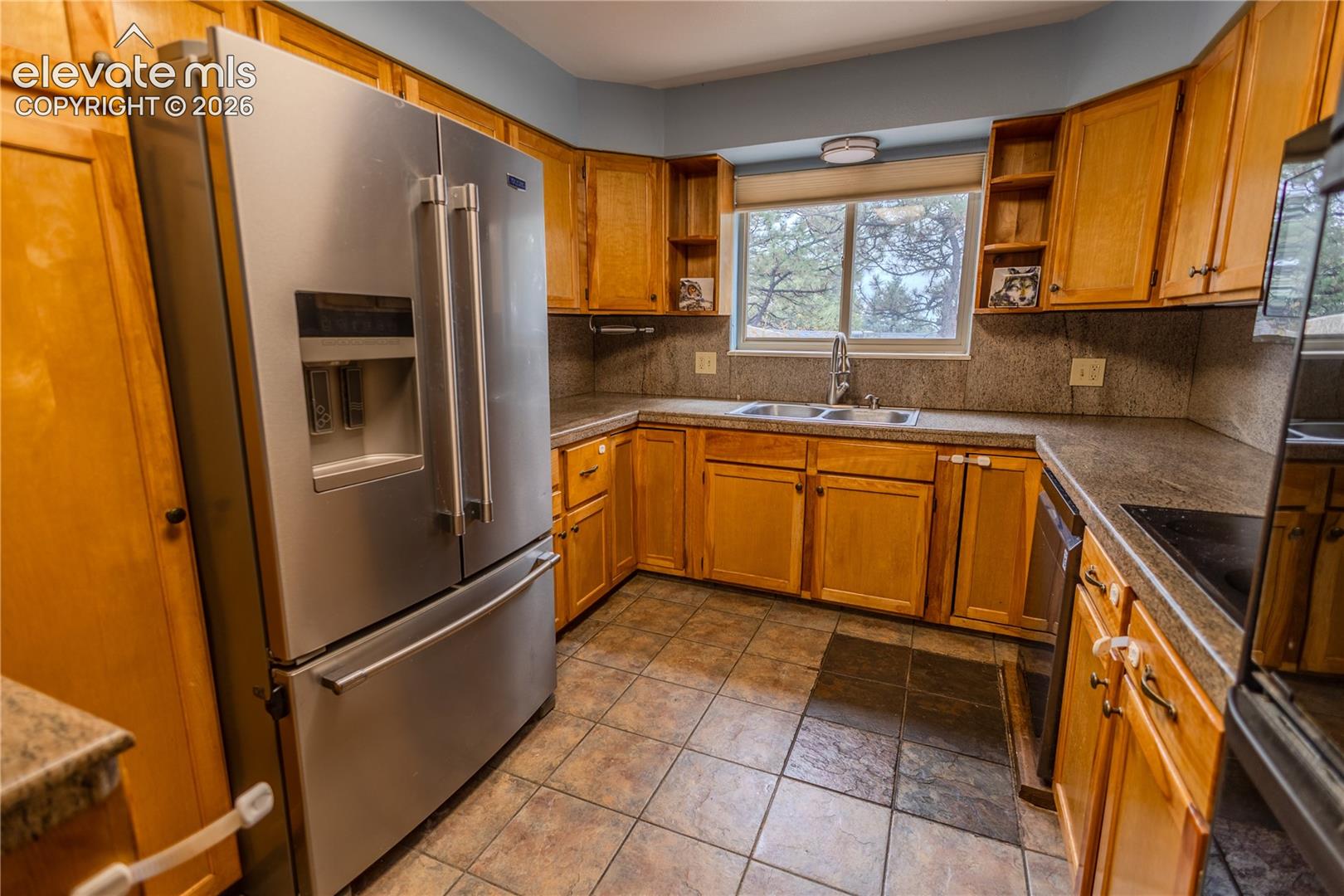 Kitchen featuring natural wood cabinetry, stone-finish countertops, stainless steel appliances, ceramic tile flooring, and a dual-basin stainless steel sink