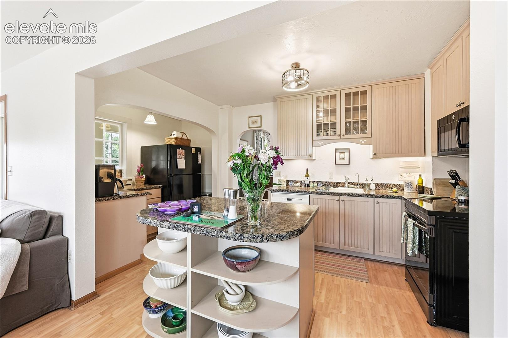 Kitchen featuring beadboard-style cabinetry, stone-finish countertops, wood-finish flooring, built-in island shelving, and glass-front upper cabinet doors
