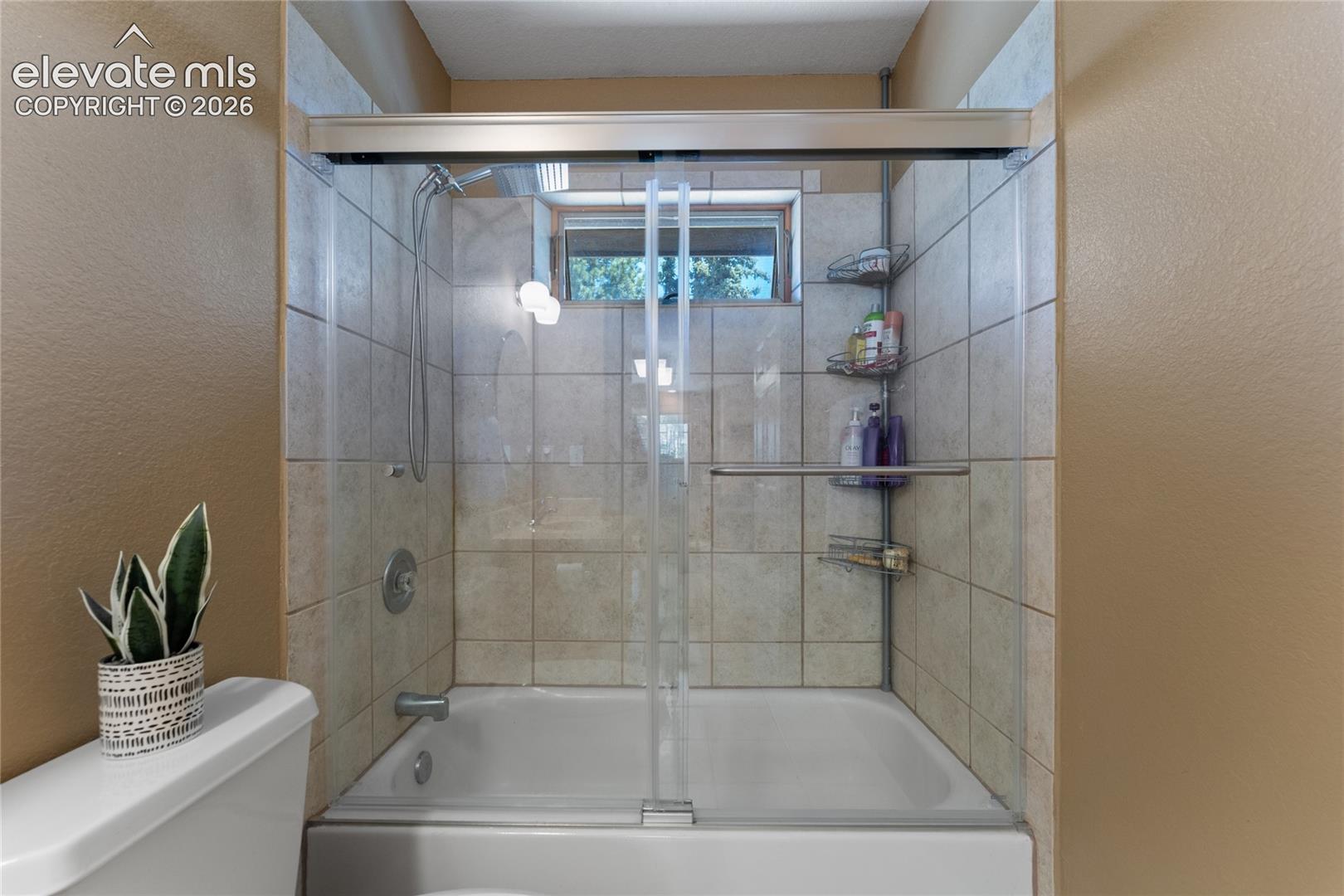 Bathtub with a glass sliding door enclosure, surrounded by light-toned tile walls