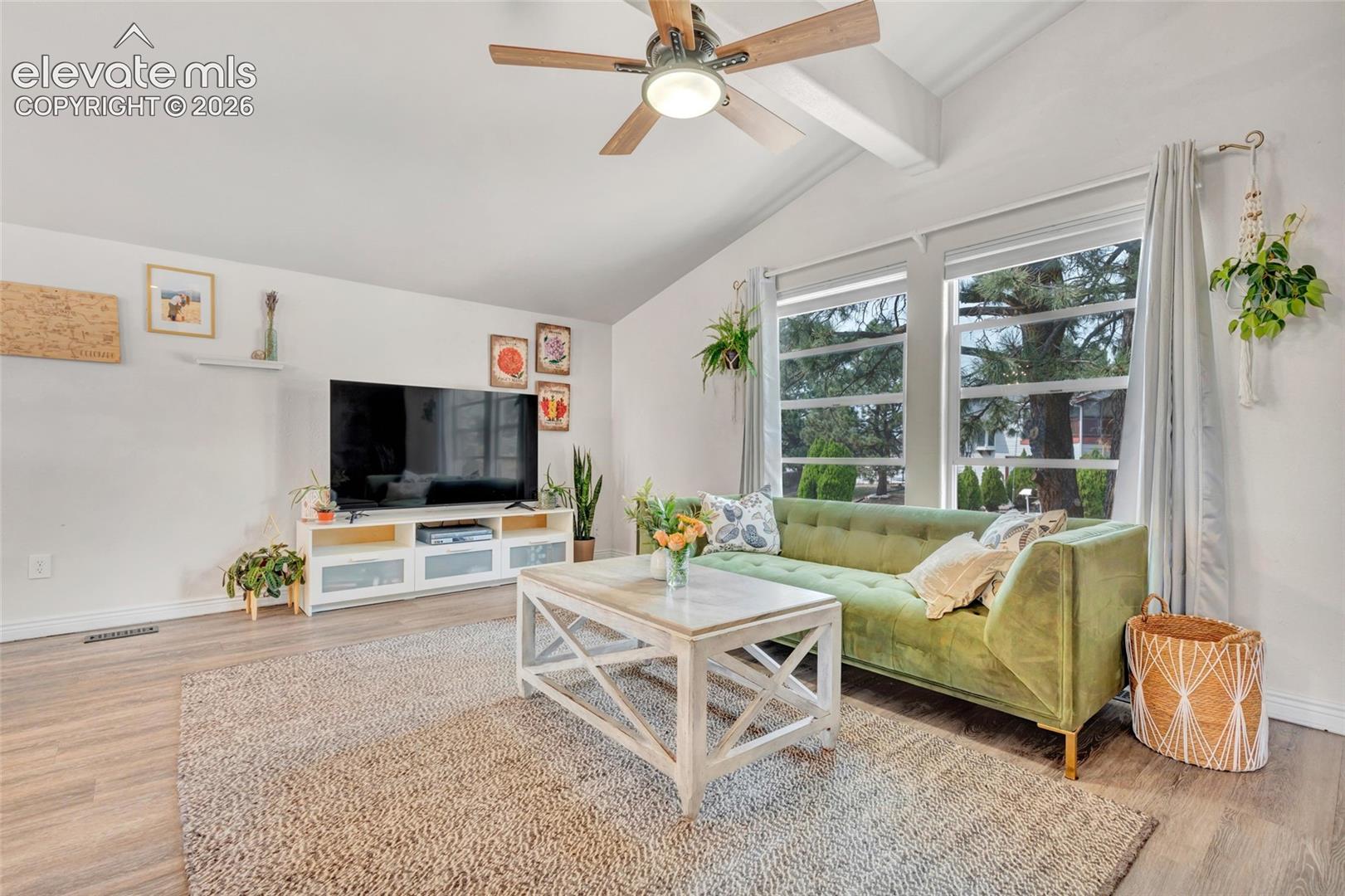 Vaulted ceilings with exposed beams and a ceiling fan, wood-finish flooring, and large windows with privacy blinds