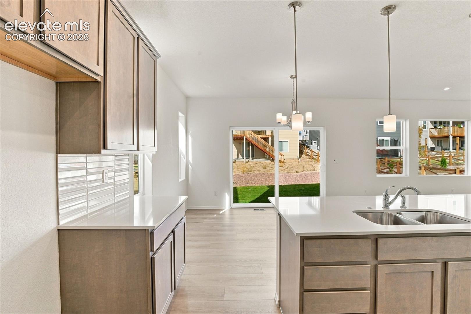 Kitchen featuring wood-finish cabinetry, quartz countertops, a horizontal tile backsplash, wood-finish flooring, and dual pendant lighting