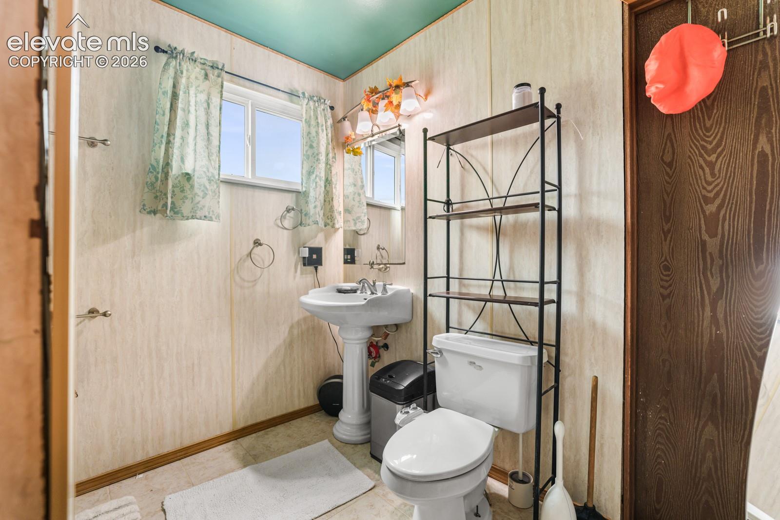 Bathroom featuring a pedestal sink, a toilet, and a window with natural light