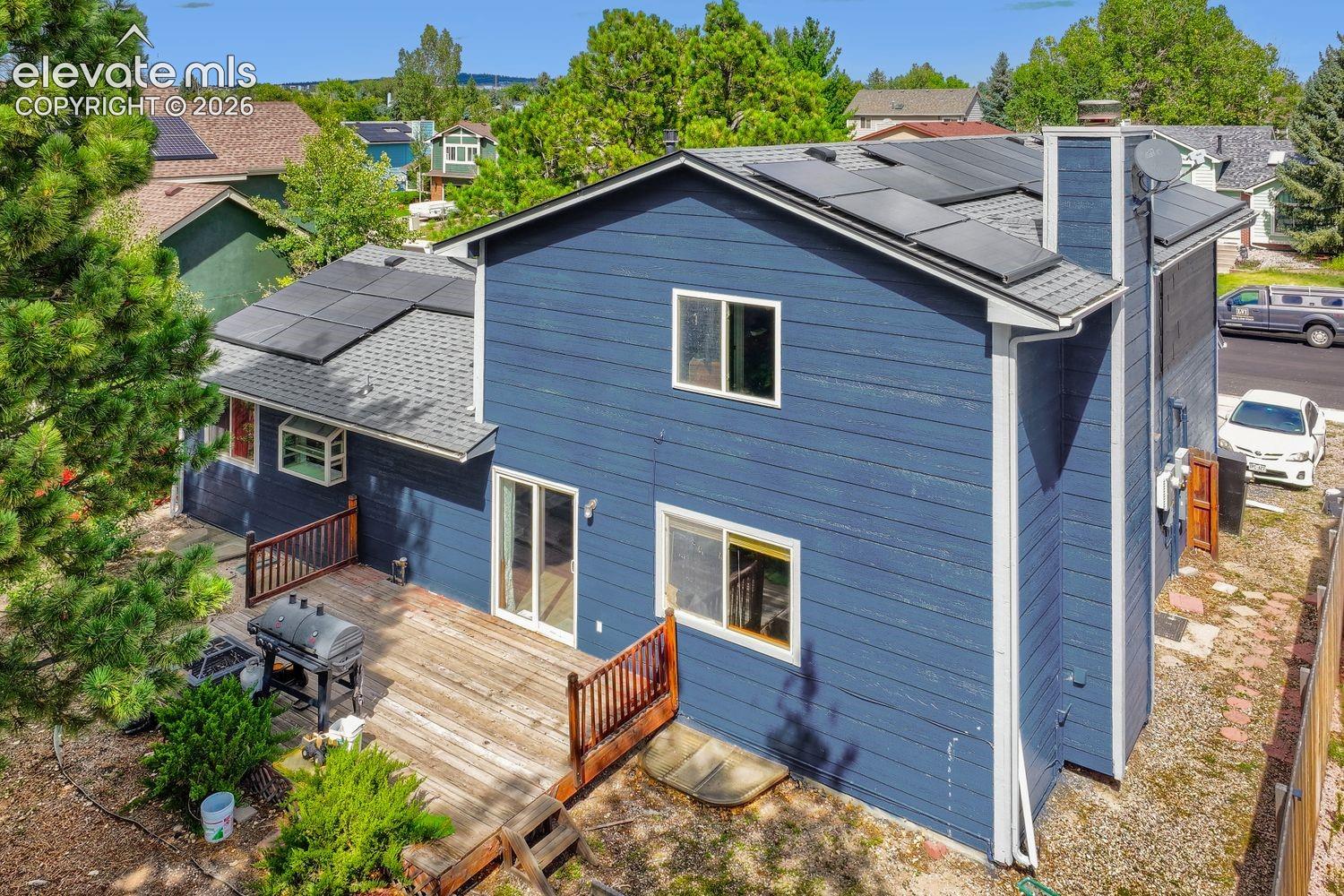 Rear exterior featuring a wood deck, sliding glass doors, multiple windows, and rooftop solar panels