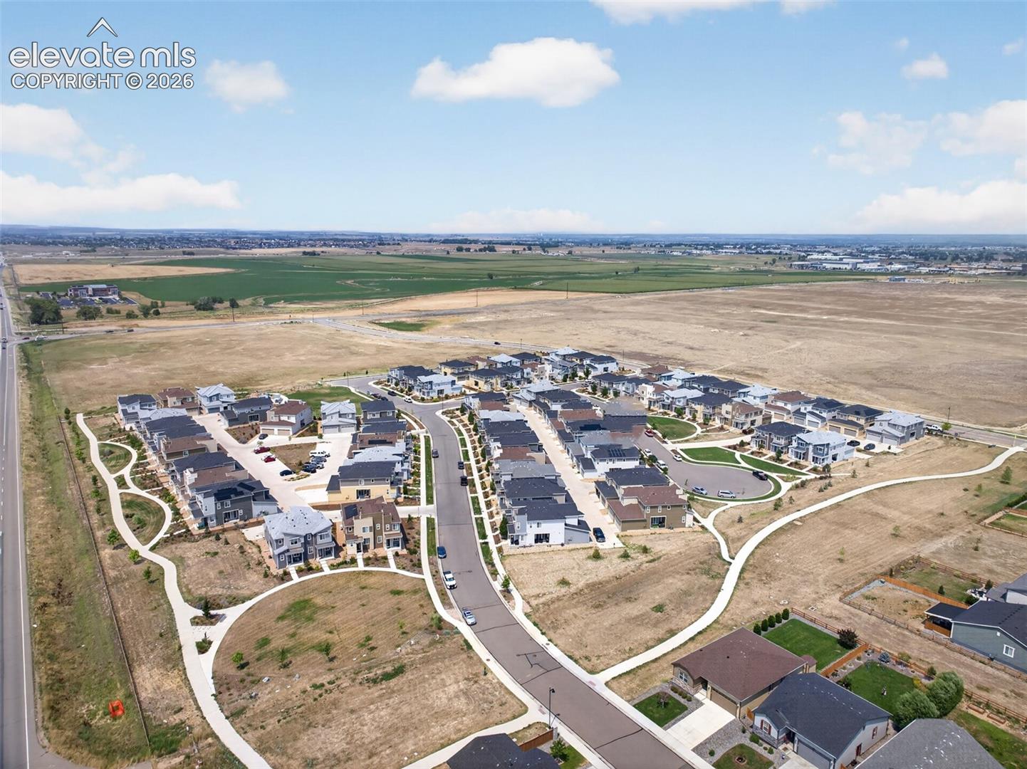 Aerial perspective of a residential development featuring curvilinear paved pathways, asphalt street infrastructure, and multiple single-family structures with dark-toned roofing materials