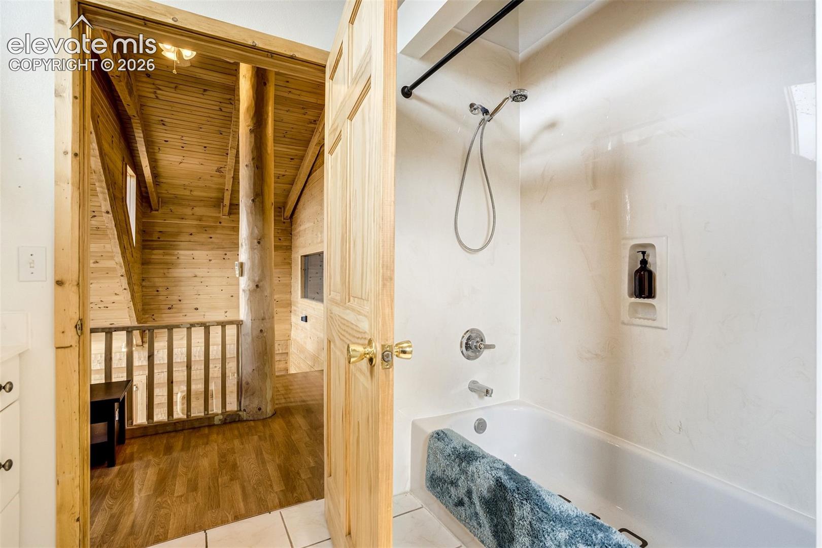 Bathroom featuring a bathtub with an integrated shower, chrome fixtures, and a recessed shower niche