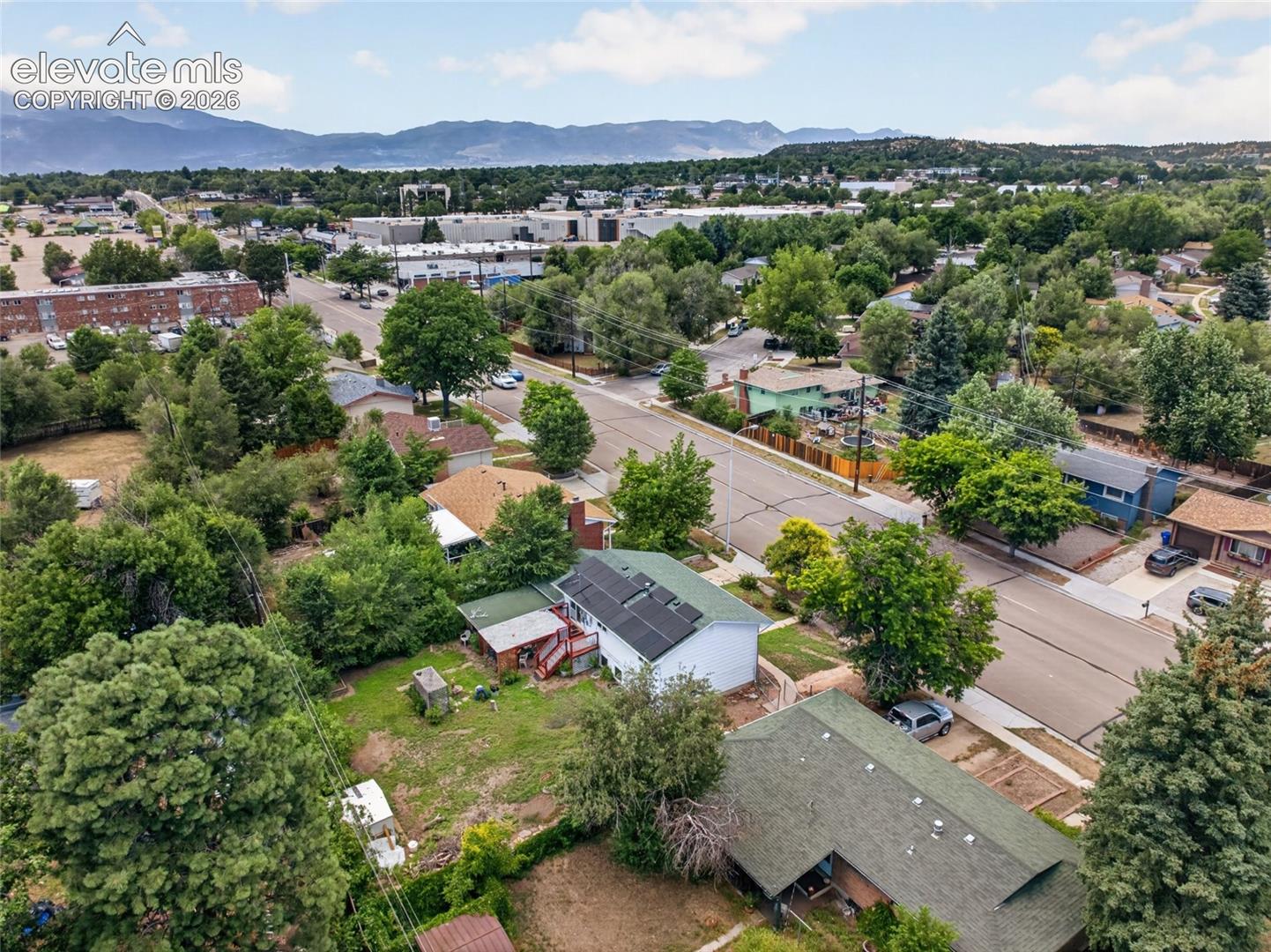 Aerial perspective featuring a detached residence with a rooftop solar panel array, attached rear deck, and mature landscaping