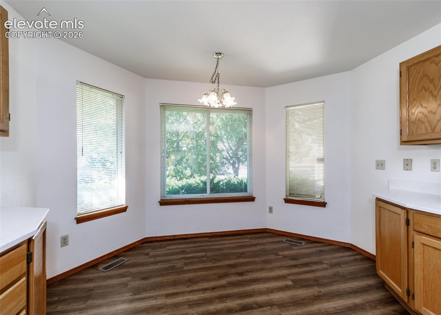 Bay window with three windows, wood-finish flooring, overhead chandelier, light wood cabinetry, and white countertops