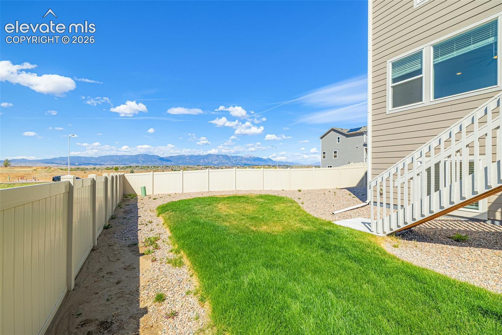 Fenced backyard with a grassy lawn, gravel landscaping, and mountain scenery
