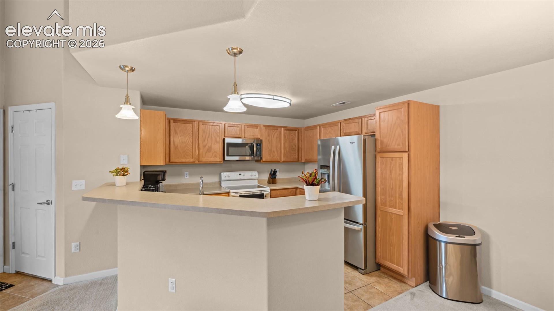 Kitchen featuring wood-finish cabinetry, stainless steel appliances, a breakfast bar, and pendant lighting