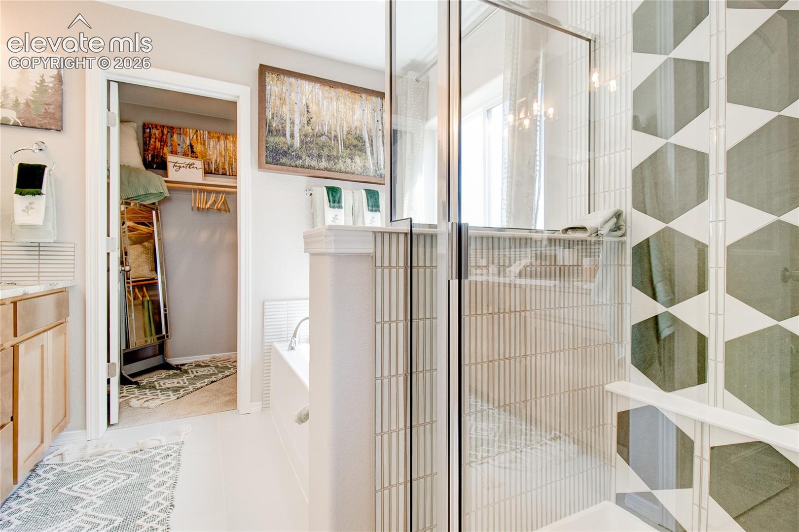 Bathroom featuring a glass-enclosed shower with geometric tile accents, a soaking tub with vertical tile surround, wood-finish cabinetry, and a walk-in closet with built-in shelving