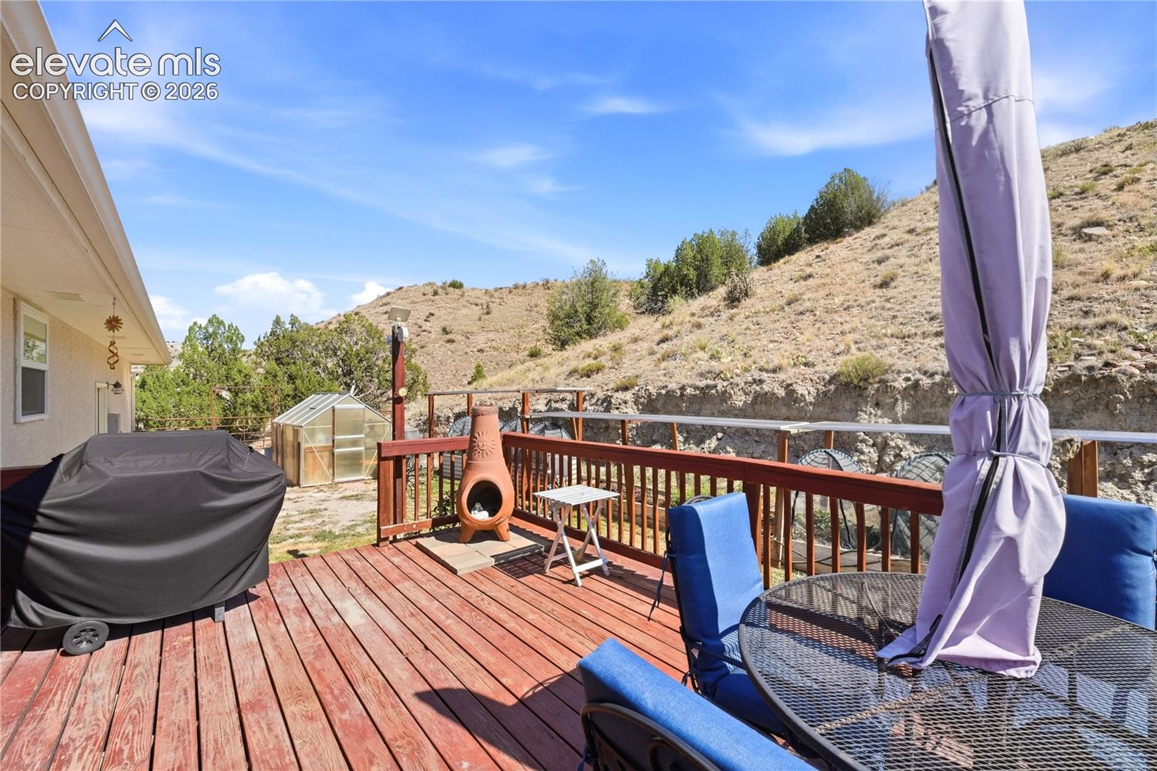 Expansive redwood deck with cable railing overlooking hillside landscape, featuring a built-in fire pit, shade sail, and lounge seating area