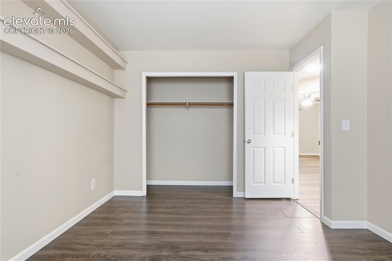 Wood-finish flooring, neutral wall color, open closet with hanging rod, white paneled door, and white trim