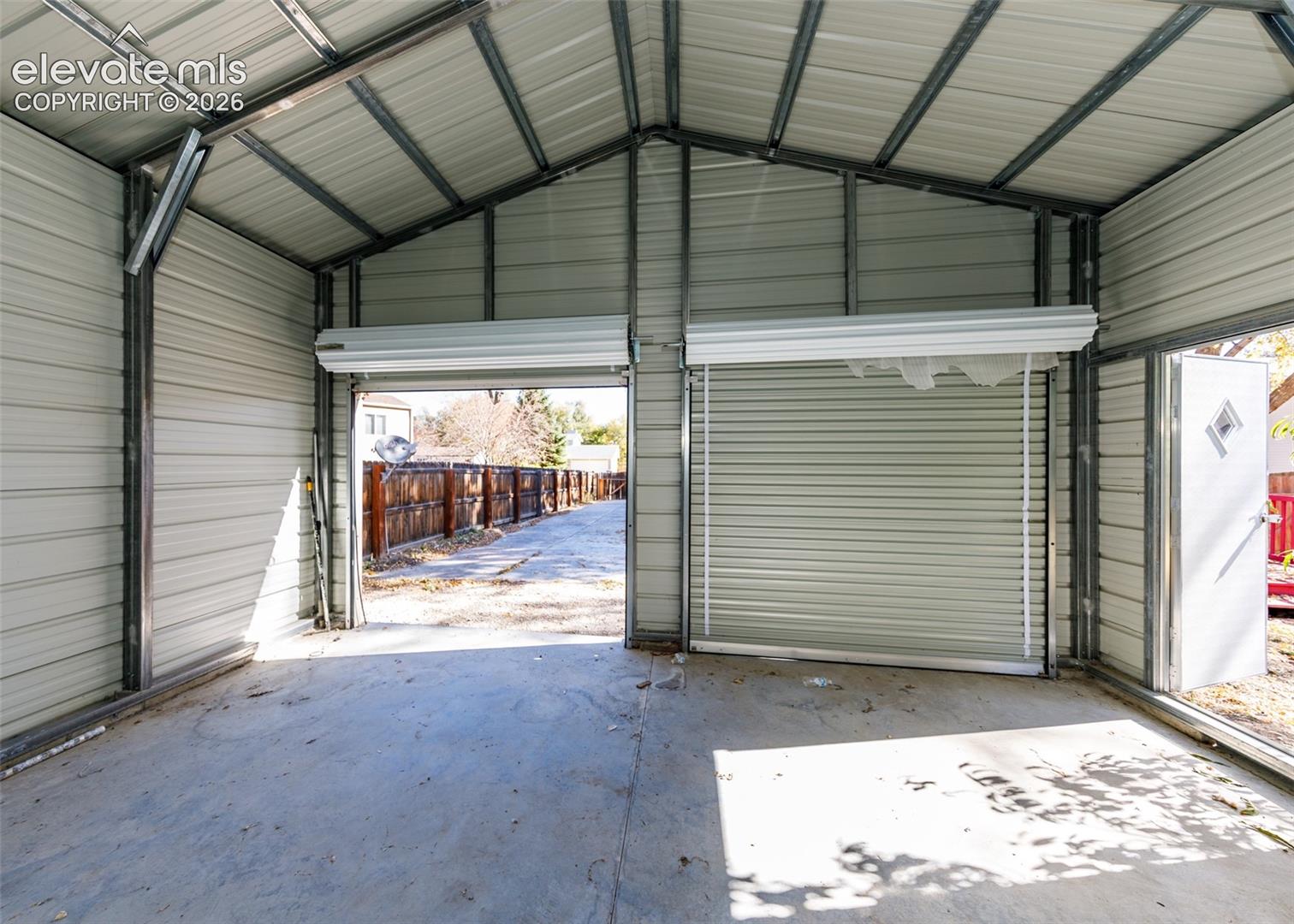 Detached metal workshop featuring exposed steel framing, dual roll-up doors, a concrete floor, and a side-entry pedestrian door
