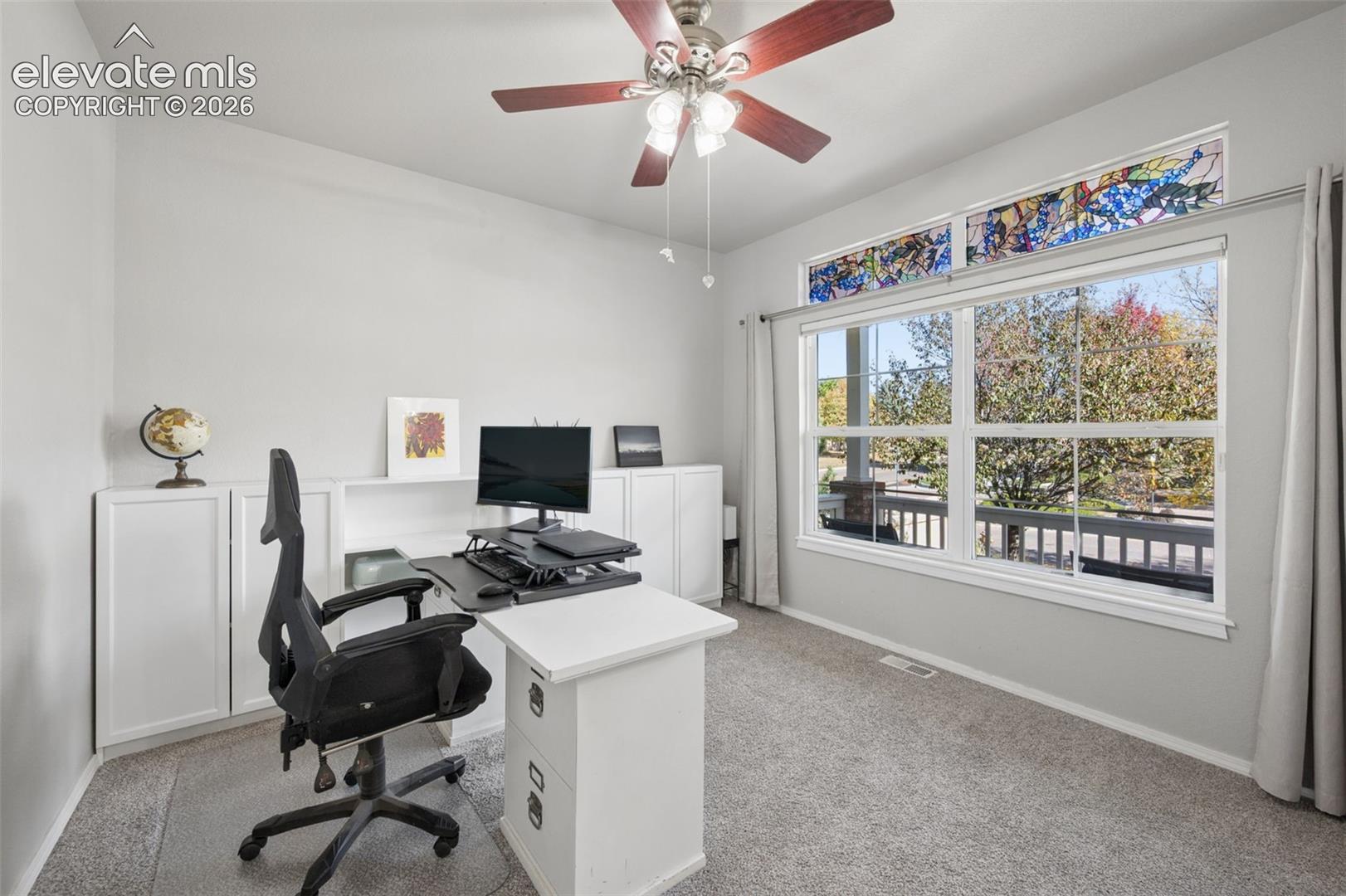 Built-in white cabinetry, stained glass transom window, ceiling fan with integrated lighting, and neutral carpeting