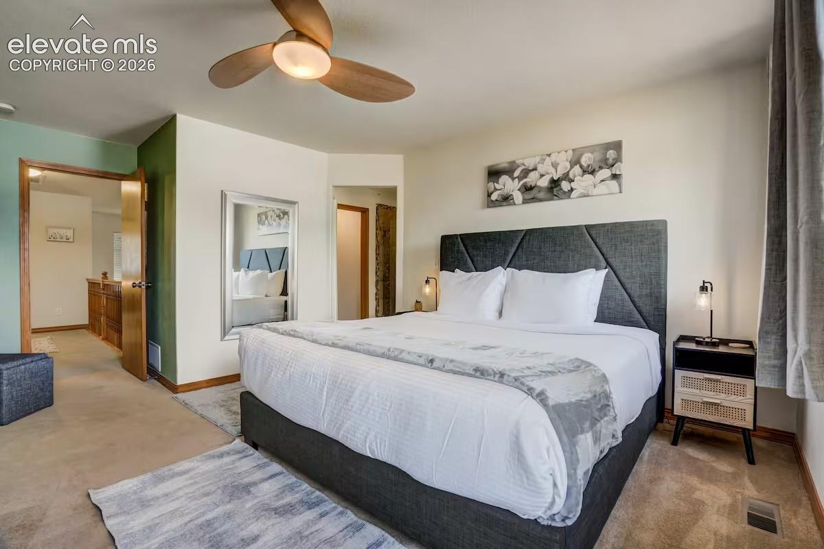 Carpeted bedroom featuring a ceiling fan with integrated lighting, a full-length mirror, and built-in wood cabinetry visible through an open doorway