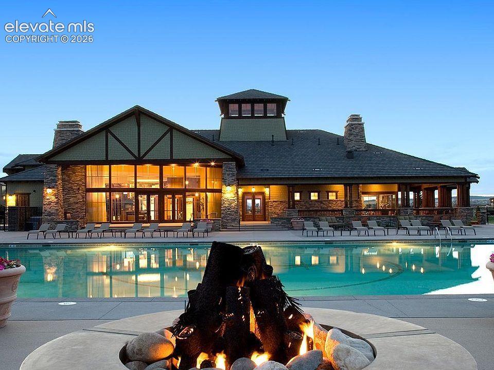 In-ground swimming pool with stone-surround fire pit, timber-frame exterior detailing, natural stone veneer siding, and expansive floor-to-ceiling window walls