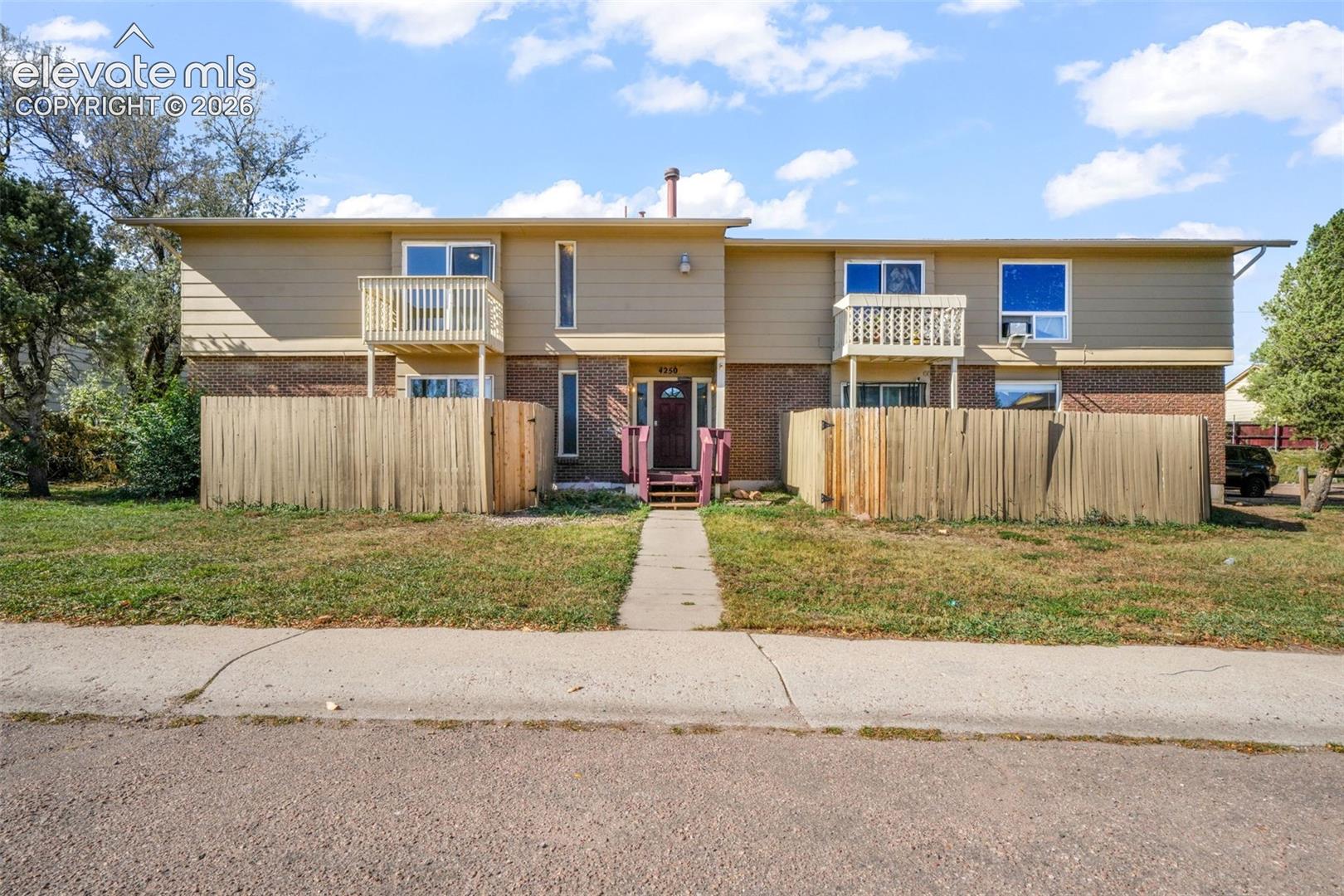 Two-story exterior featuring a brick and horizontal siding façade, two upper-level balconies with wood railings, and fenced outdoor spaces