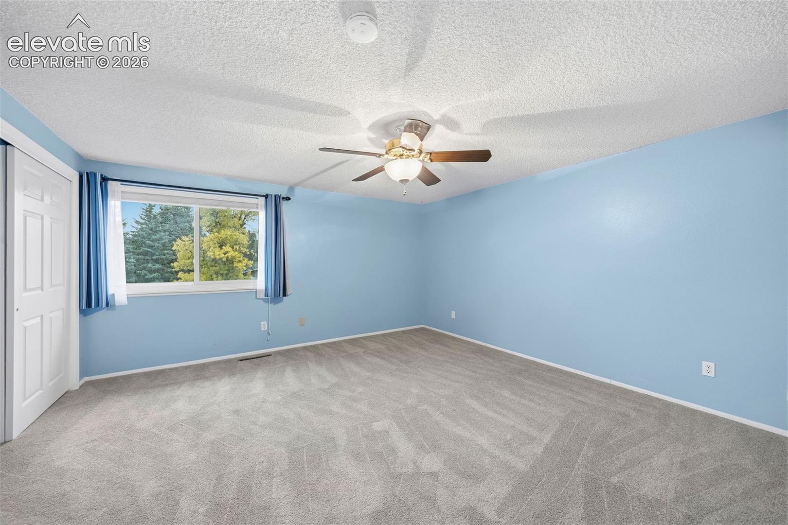 Room featuring neutral carpet, textured ceiling, central light fixture with ceiling fan, and sliding door closet