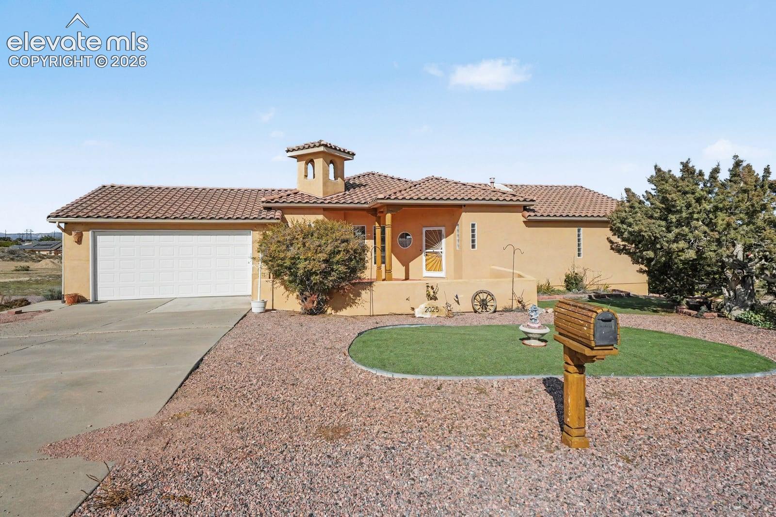Stucco exterior residence featuring a tile roof, decorative cupola, attached two-car garage, and desert-inspired hardscaping