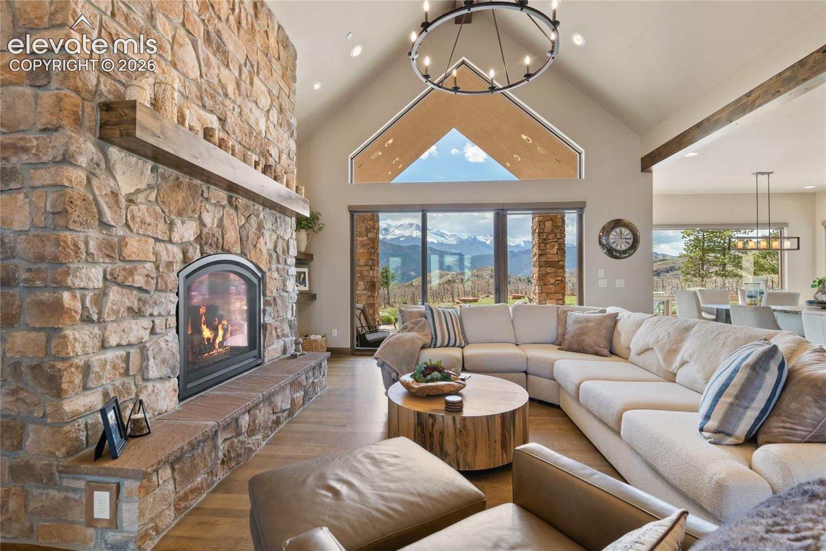 Soaring vaulted great room with floor-to-ceiling stone gas fireplace, white oak floors, and panoramic Pikes Peak views.