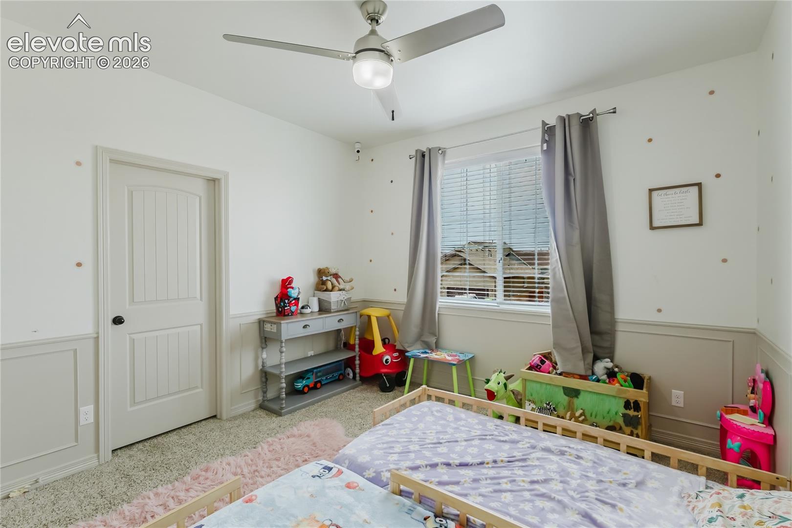 Carpeted interior room featuring wainscoting, a ceiling fan with integrated lighting, and a window with horizontal blinds