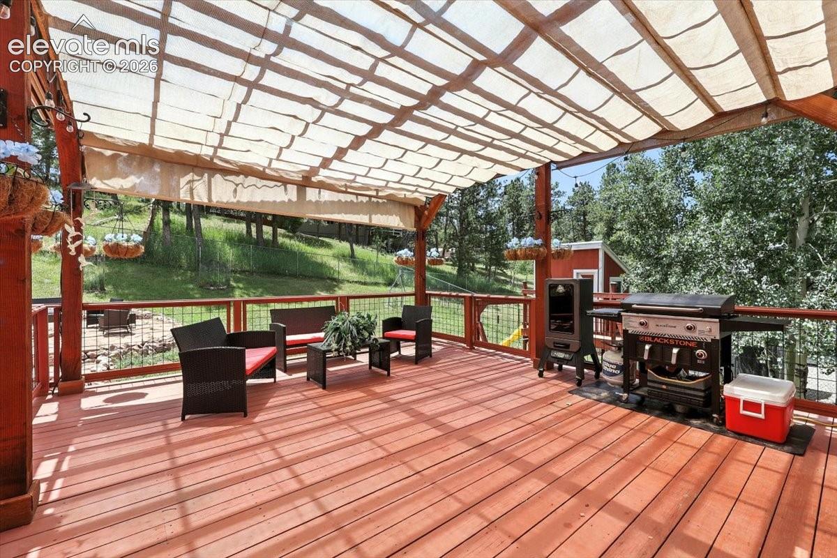 Spacious wooden deck featuring a retractable fabric canopy, custom pergola structure, and wire-grid perimeter railing