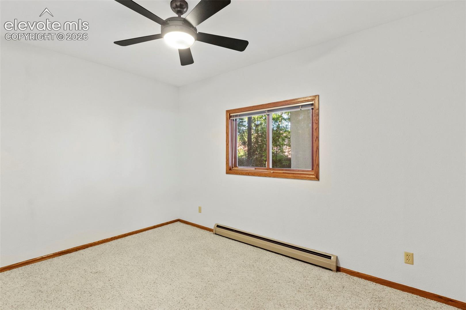 Neutral-toned interior space featuring carpeting, a multi-blade ceiling fan with integrated lighting, and a window framed in wood-finish trim