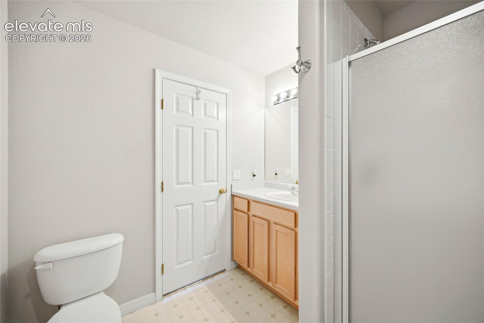 Bathroom featuring a light-finish wood vanity, integrated sink, wall-mounted vanity lighting, shower with a sliding frosted glass enclosure, and tile flooring
