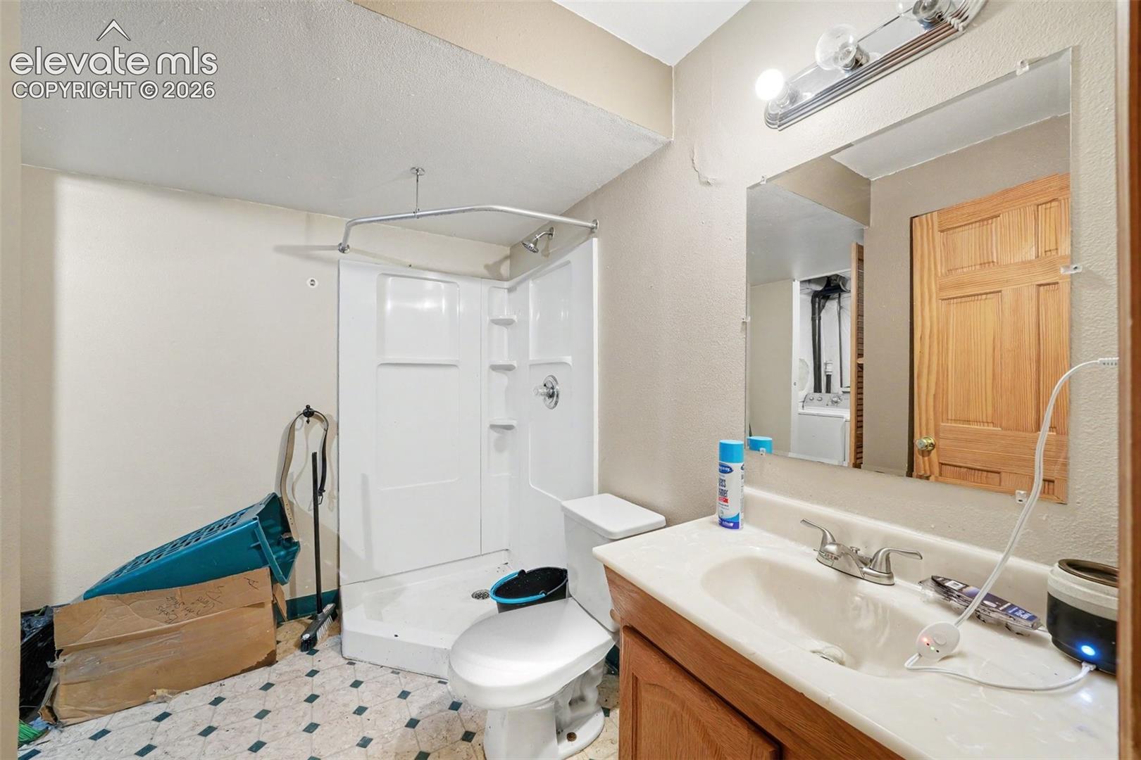 Bathroom featuring a white molded shower stall, wood-finish vanity cabinet, integrated sink with dual-handle faucet, and wall-mounted vanity lighting