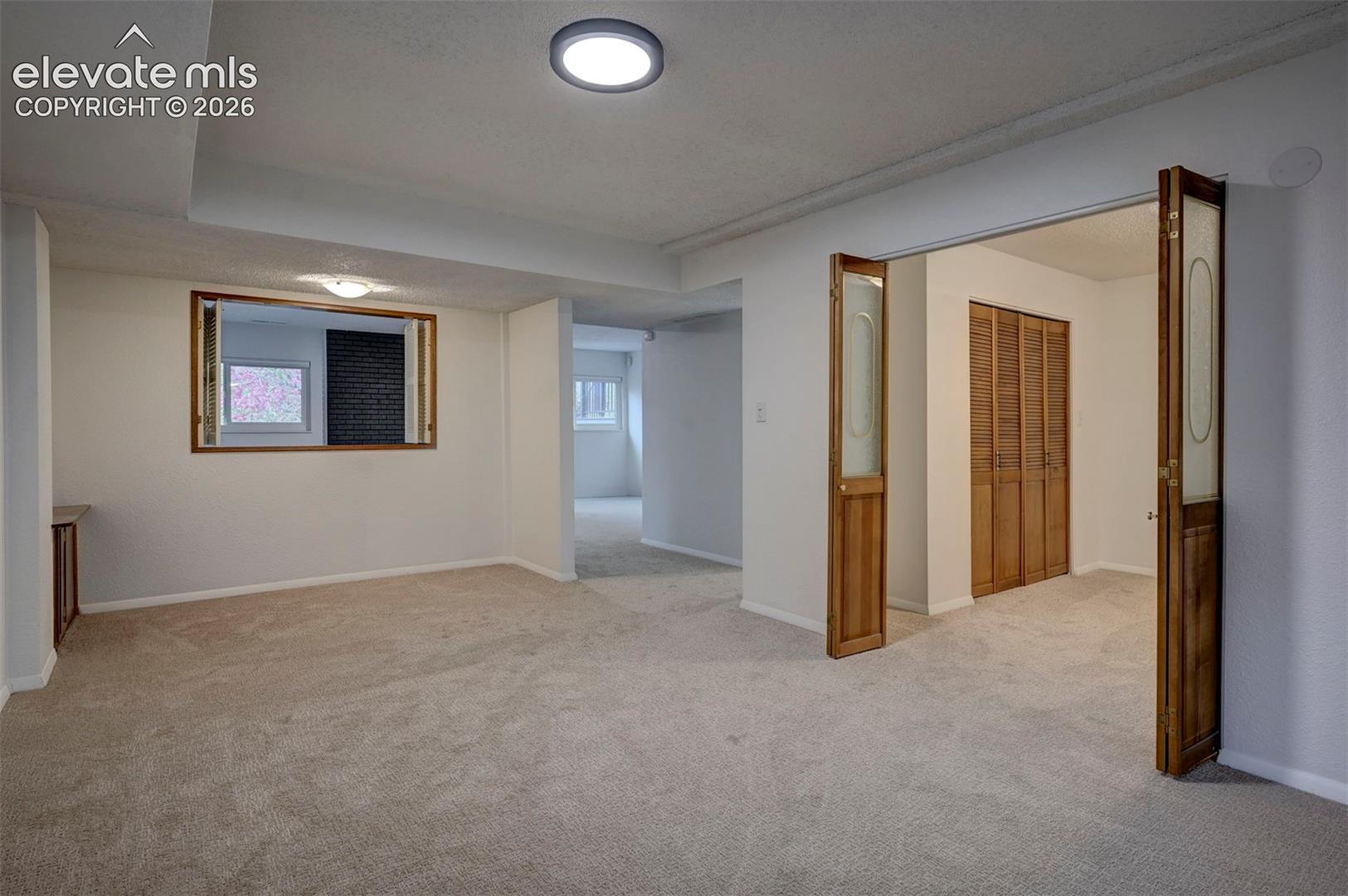 Neutral-toned wall-to-wall carpeting, recessed ceiling lighting, louvered wooden closet doors, and wood-framed interior glass French doors