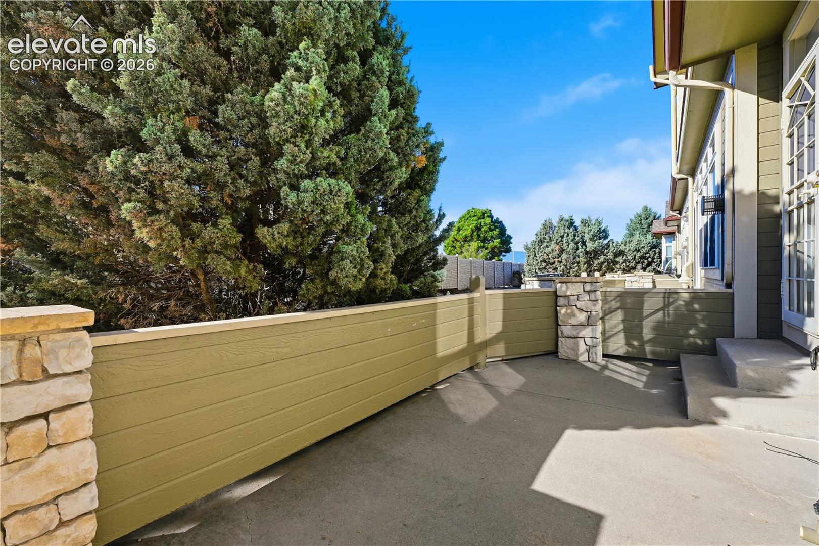 Private patio featuring concrete flooring, horizontal wood-paneled privacy fencing, and stone pillar accents